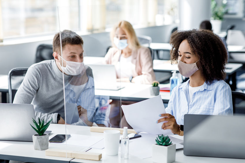 employees in office wearing face masks, separated by partition